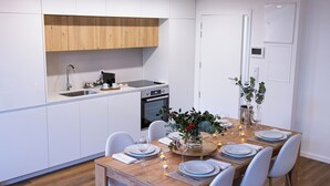 Una cocina moderna con armarios blancos, encimera de madera y un comedor preparado para seis personas con mesa de madera, sillas blancas y un centro de mesa.