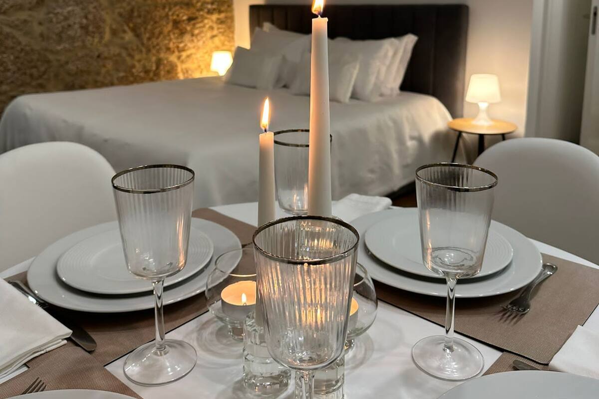 Une table à manger élégamment dressée, avec des bougies, des verres et des assiettes, dans une chambre d’hôtel dotée d’un mur en pierre et d’un lit en arrière-plan.