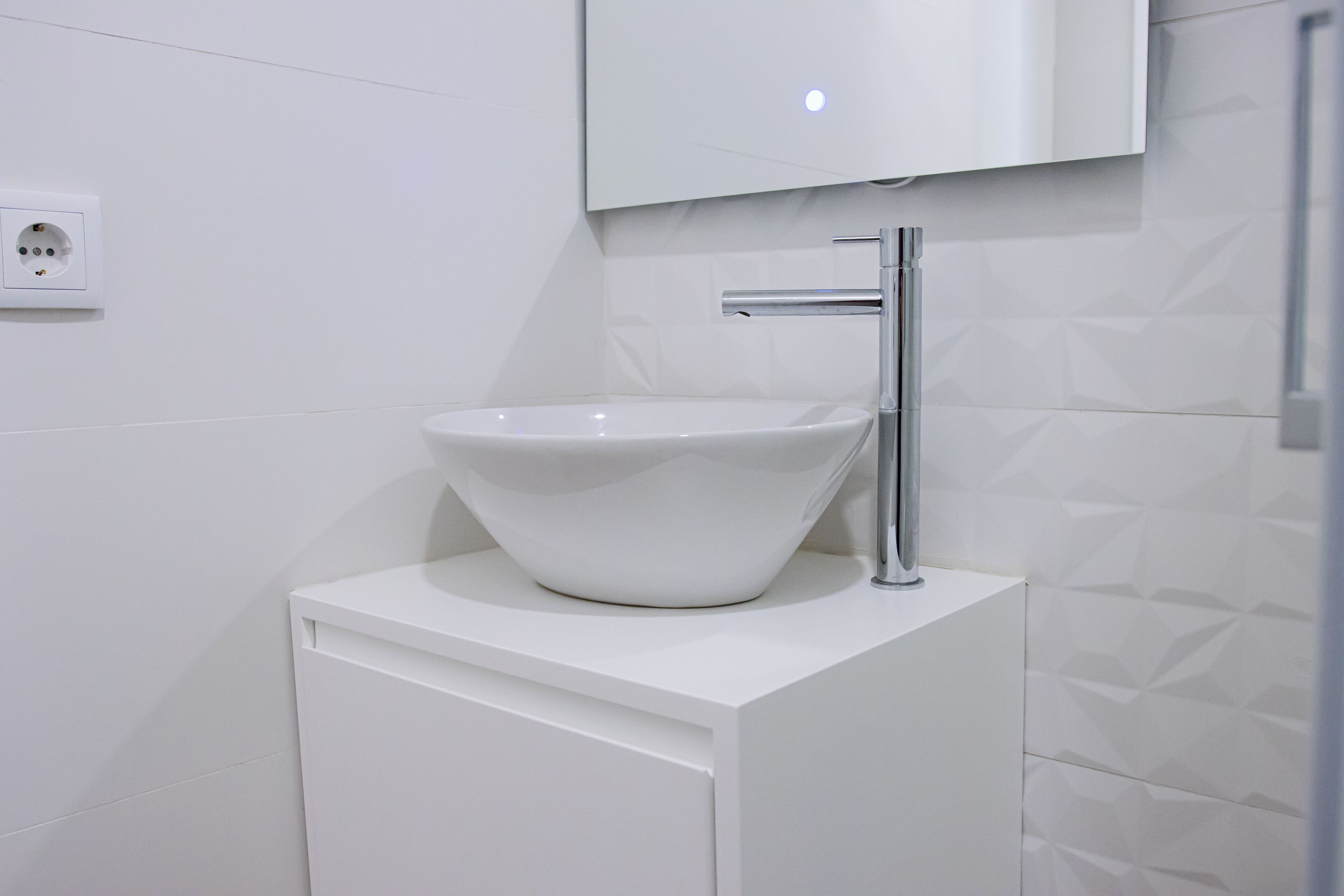 Un baño moderno con lavamanos blanco, grifo cromado y espejo montado en la pared.