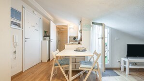Een kleine keuken met een eettafel, stoelen, een televisie en een kleine koelkast.