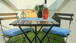Een terras buiten met een tafel, twee stoelen, een fles en een glas.