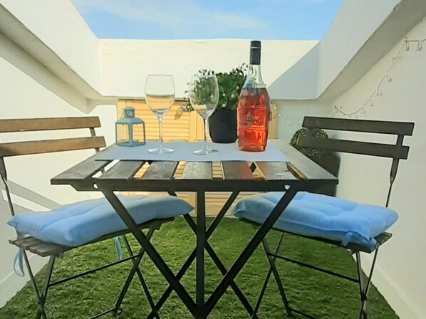 An outdoor patio with a table, two chairs, a bottle, and a glass.