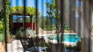 Ein Poolbereich mit freier Sicht auf den Pool, eine Pergola mit Kletterpflanzen und eine rote Struktur im Hintergrund.