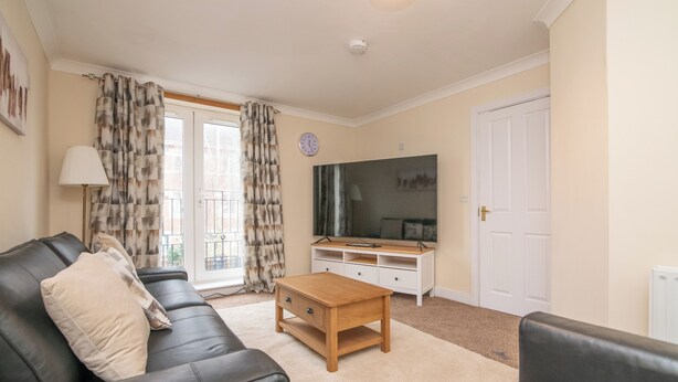 A living room with a black leather sofa, a wooden coffee table, a TV on a white stand, and a white door. - Newly refurbed 5 bed house with Free Parking n Dryer (Birmingham)