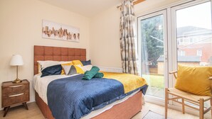 A bedroom with a bed, a nightstand, a chair, and a window with a view of a house. - Newly refurbed 5 bed house with Free Parking n Dryer (Birmingham)