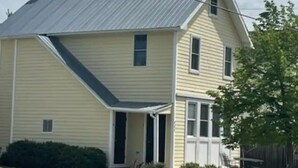 A single-story house with a gabled roof, a front porch, and a small front yard with a tree and a bench. - Historic Chesapeake City Stay   (Chesapeake City)