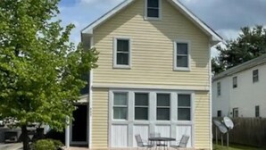 A two-story house with a front porch, a garage, and a small patio area with outdoor furniture. - Historic Chesapeake City Stay   (Chesapeake City)