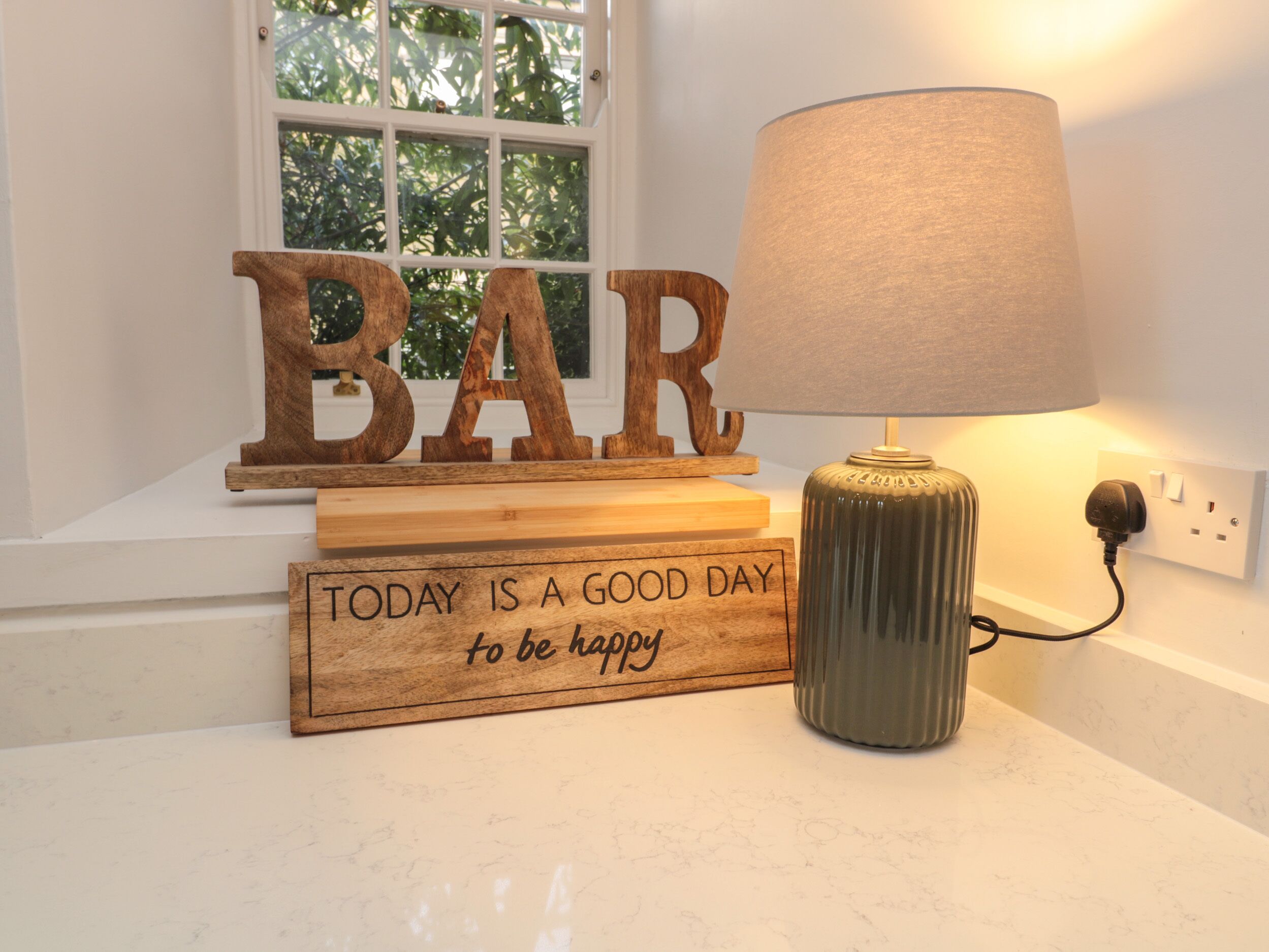 A wooden sign with the word "BAR" and another sign saying "TODAY IS A GOOD DAY to be happy." A lamp is on the table beside them.