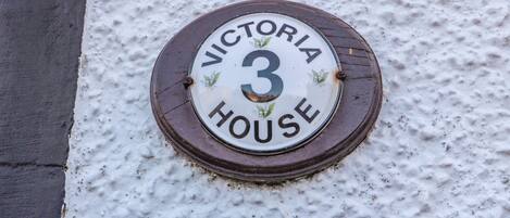 A house number plaque on a textured wall, indicating "VICTORIA HOUSE 3".
