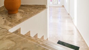A hallway with a marble floor, a potted plant, and a door with a stained glass window. - Maela Luxury Suite (Hersonissos)