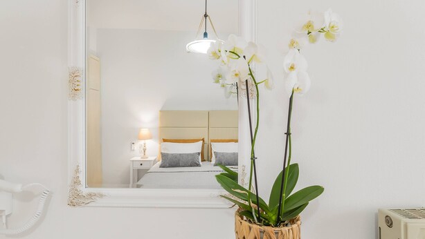 A bedroom with a bed, bedside table, lamp, and a mirror reflecting the room. - Maela Luxury Suite (Hersonissos)