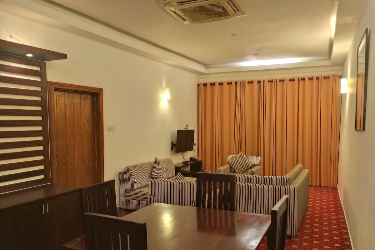 A room with a dining table, chairs, striped sofas, a TV, and curtains.