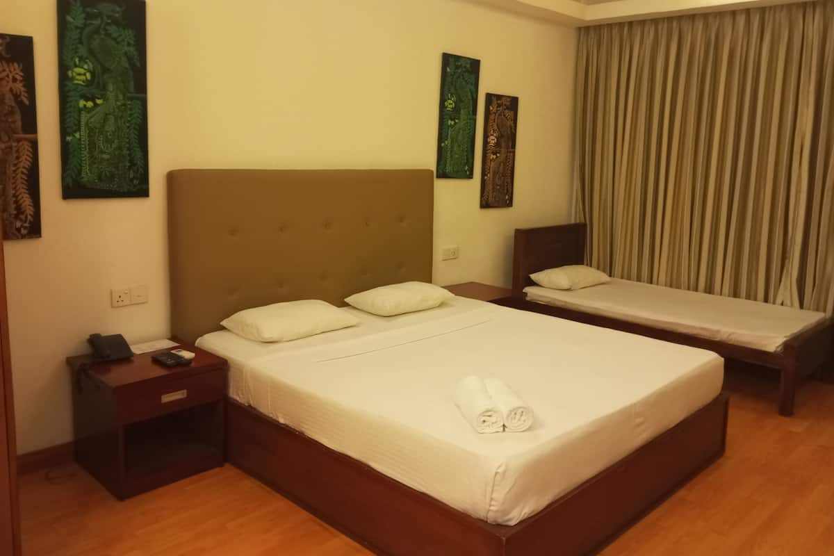 A hotel room with two single beds, a large bed, a nightstand with a phone, and artwork on the walls.