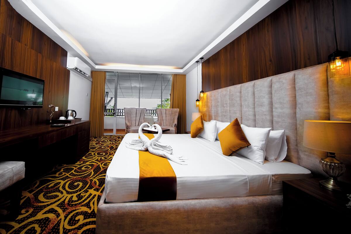 A hotel room with a large bed, a TV, a desk, and a view of the outdoors.