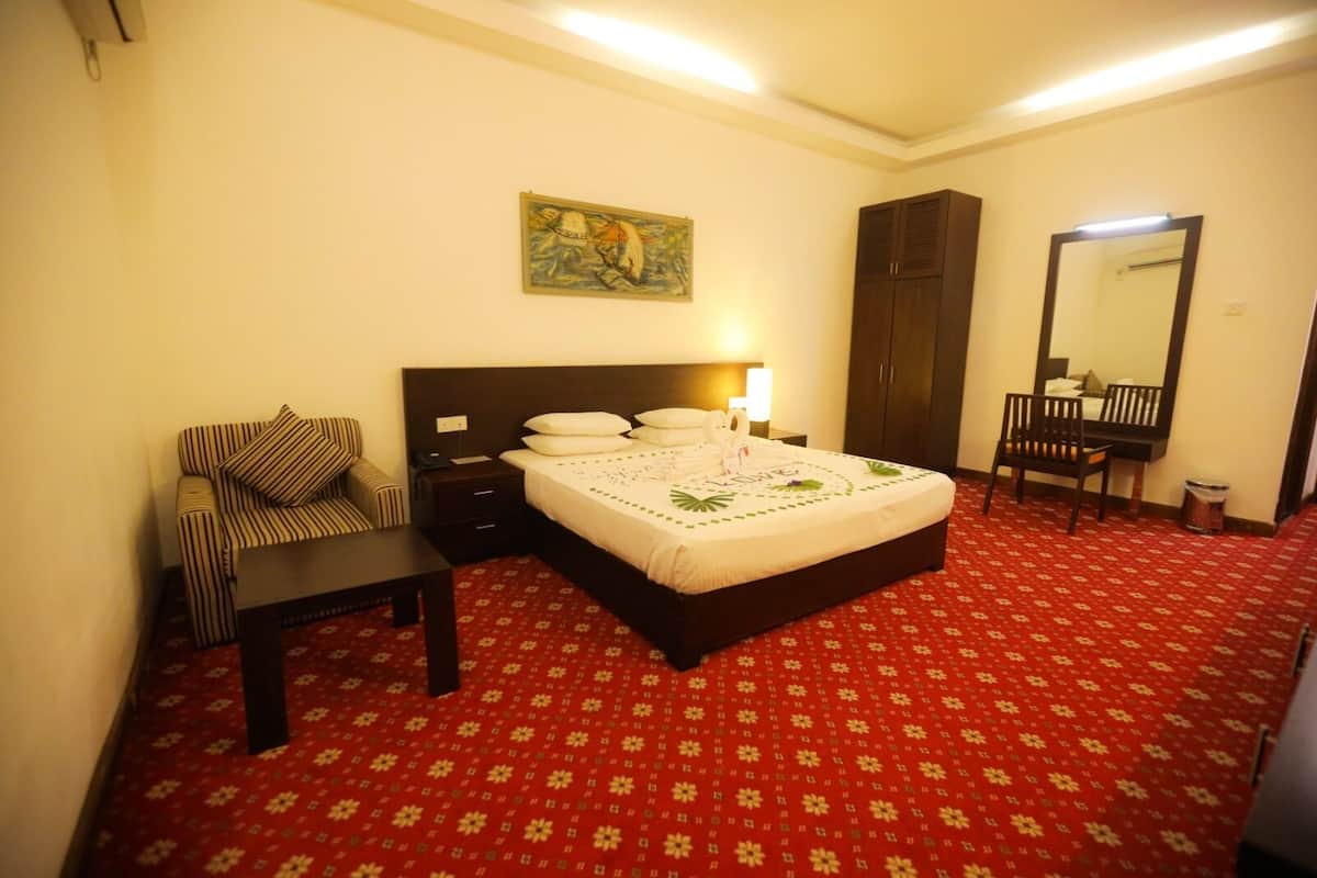 A hotel room with a bed, a chair, a desk, a wardrobe, and a mirror.