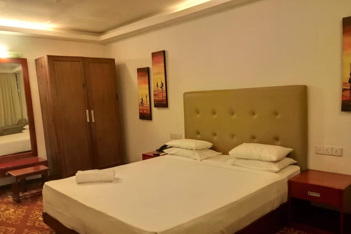 A hotel room with a large bed, a wooden wardrobe, a bedside table, and a mirror.
