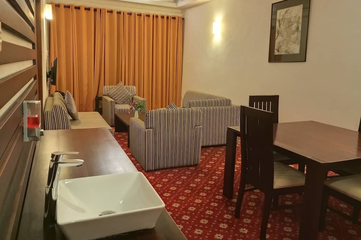 A hotel room with a dining area, a sofa set, a table with chairs, a white sink, and a red patterned carpet.