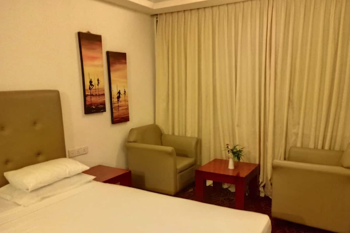 A hotel room with a large bed, two armchairs, a small table with a vase, and two wall art pieces.