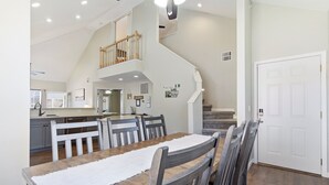 Uma sala de jantar espaçosa com uma mesa e cadeiras de madeira, cozinha ao fundo e uma escada que dá para um andar superior.