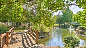 A wooden bridge over a pond with a fountain, surrounded by lush greenery and a stone wall. - Waterfront Condo near Marina (Branson)