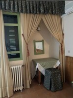 Una habitación pequeña y acogedora, con cama, radiador y ventana con cortinas.