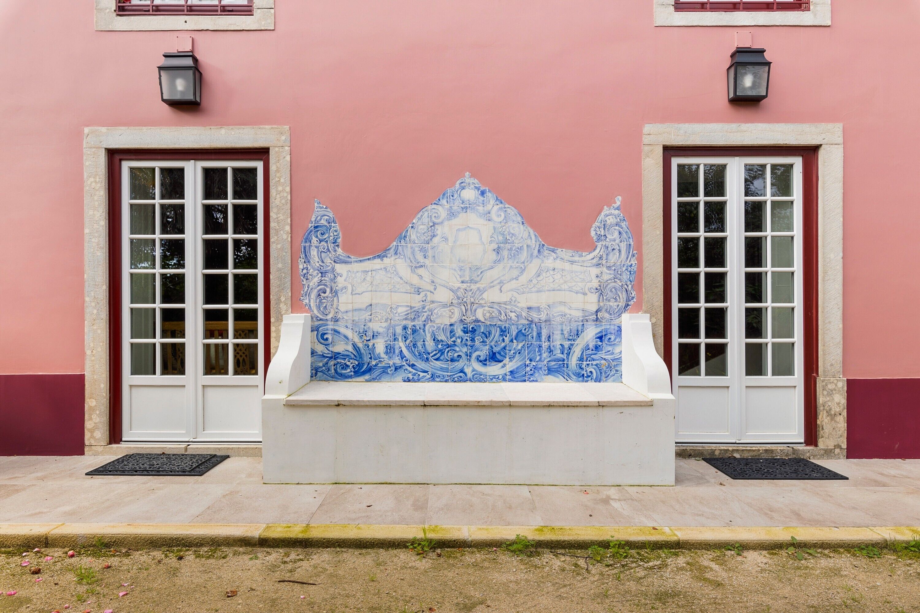 Un edificio con fachada rosa, dos puertas blancas con marcos rojos y una estructura central con azulejos azules y blancos.