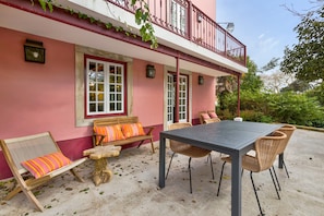 Um edifício rosa com varanda, área externa para sentar e uma mesa com cadeiras.