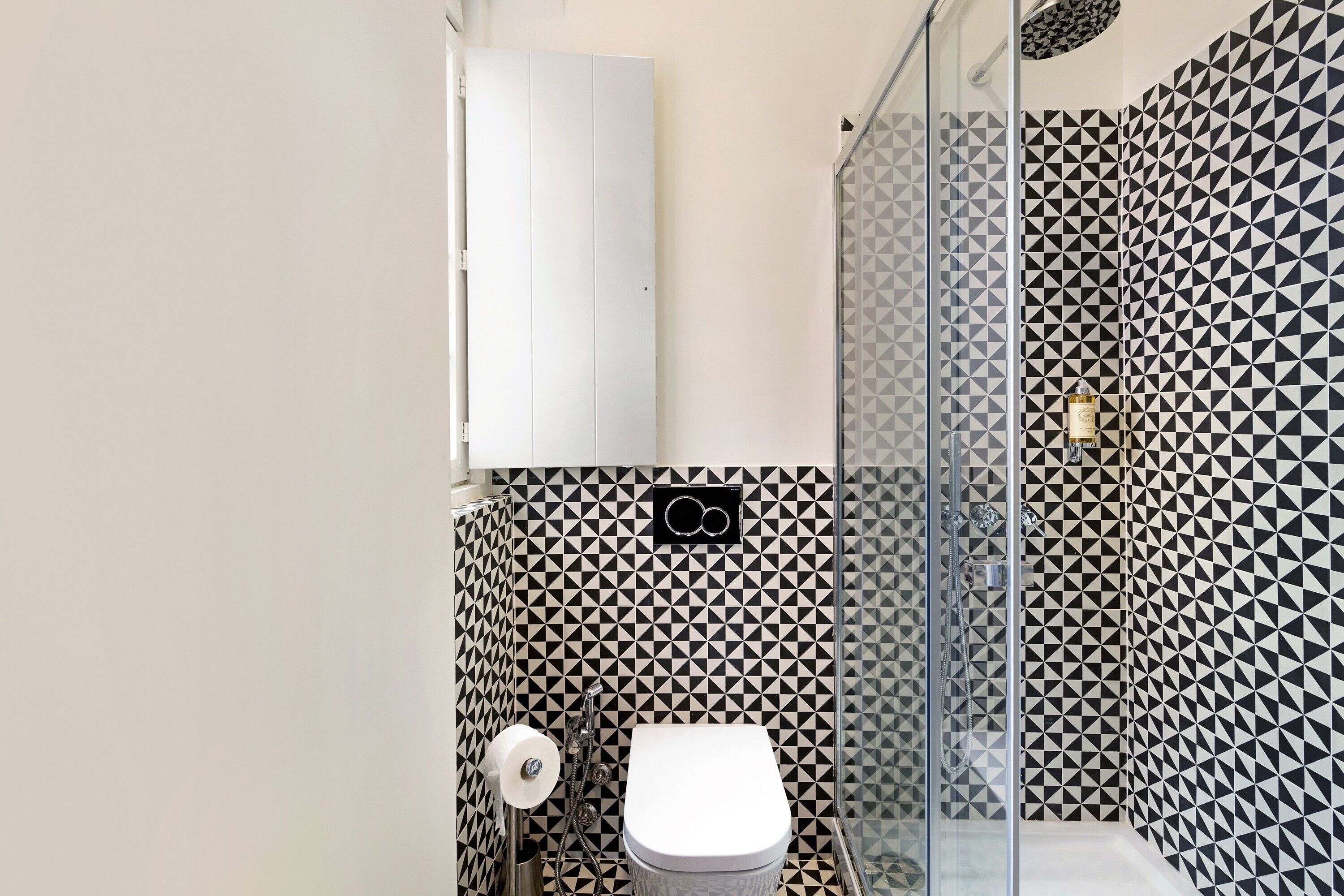 A bathroom with a geometric patterned wall, a toilet, and a glass shower enclosure.