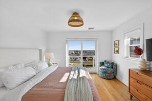 Un dormitorio con cama, cómoda, silla y ventana con vista a casas.