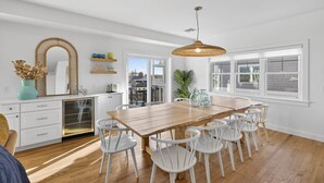 Una cocina amplia con una mesa de madera y sillas blancas, un espejo grande y una lámpara colgante.