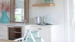 Una cocina con armarios blancos, encimera de madera y una lámpara colgante de fibras naturales.