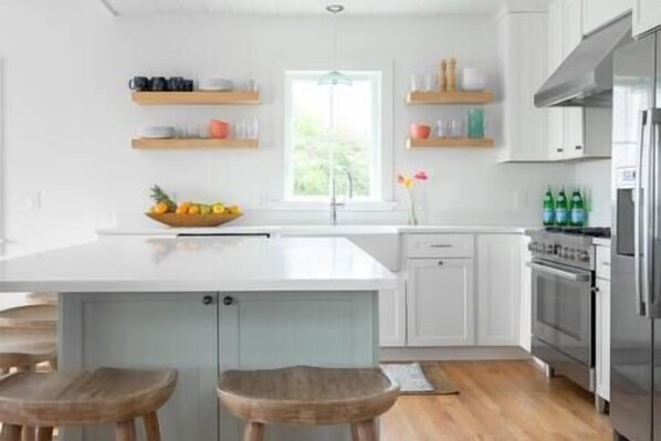 Una cocina moderna con muebles blancos, una isla central con taburetes y un ventanal que proporciona luz natural.