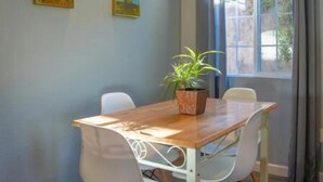 A dining area with a wooden table and white chairs, a potted plant, and two paintings on the wall. - Relaxing Home With SF Bay View

 (Millbrae)