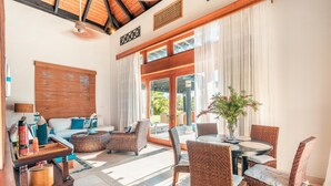 A spacious living area with a sofa, wicker chairs, a dining table, and a large window with curtains. - Bungallow With Private Backyard and Pool (Punta Cana)