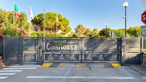 Een toegangspoort met aanduiding 'Camunione Residence CalaRossa', een stopbord en vlaggen.