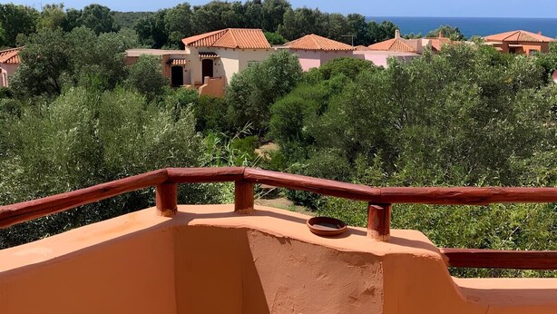 Een balkon met uitzicht op gebouwen met terracottadaken en begroeiing.