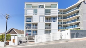 A multi-story building with balconies, a gated entrance, and a clear sky.
