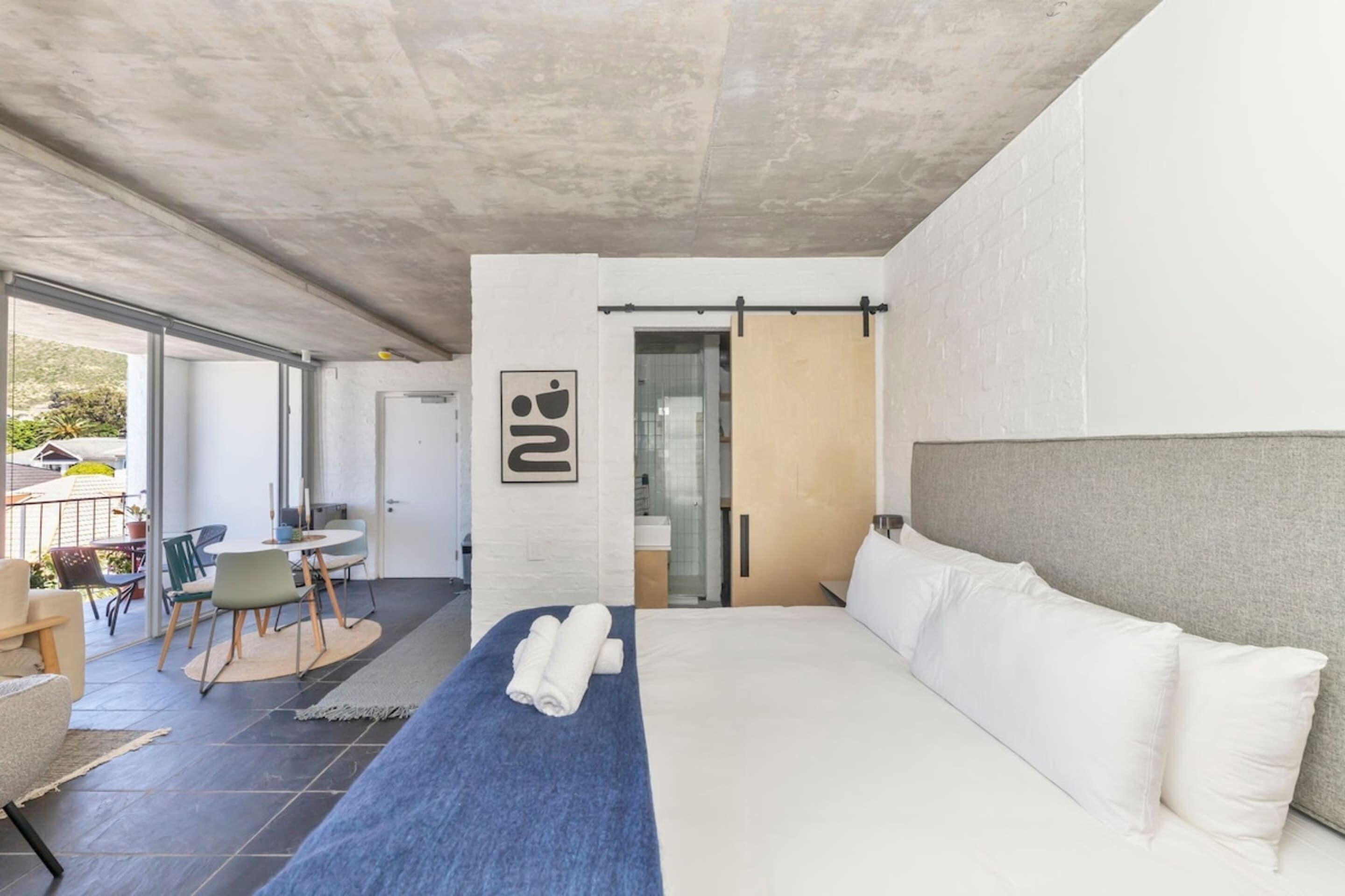 Una habitación de hotel moderna con una cama grande, un escritorio pequeño y una puerta corrediza de cristal que da a un balcón.