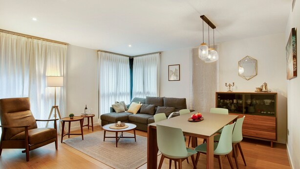 Ein modernes Wohnzimmer mit einer Couch, einem Esstisch, Stühlen, einer Lampe und einem Schrank.