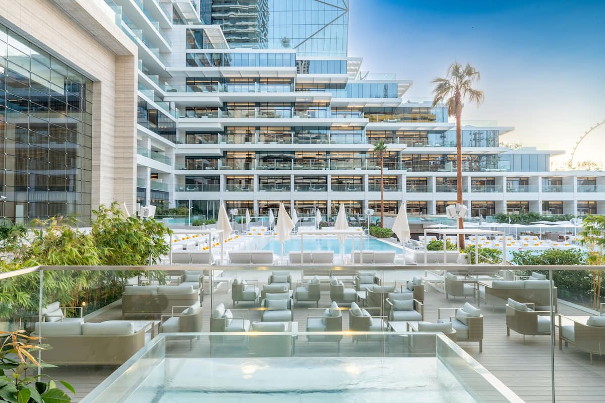 Un hotel moderno con piscina en la azotea, varios balcones y fachada de vidrio.