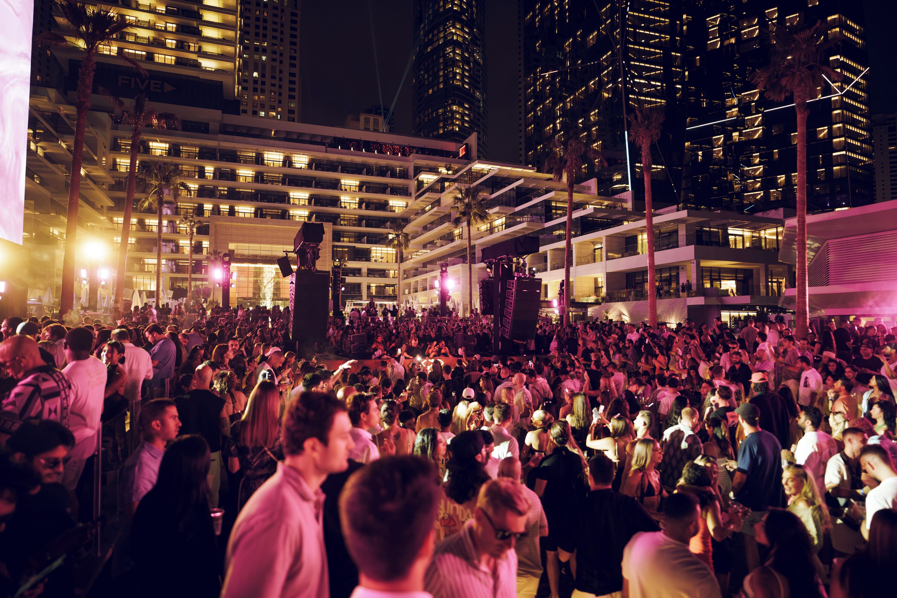 A crowded urban night scene with tall buildings and palm trees.