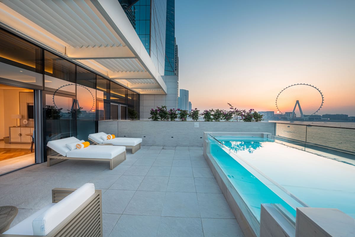 Un área de piscina en la azotea con sillones de descanso y vistas a una noria.