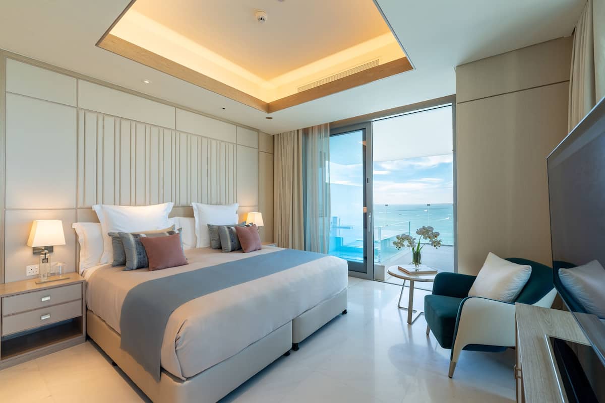 Una habitación de hotel moderna con una cama grande, un rincón de descanso y vistas al océano, además de un balcón.
