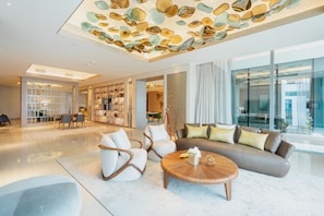 A spacious living area with a large sofa, two armchairs, and a coffee table. There is a ceiling with a decorative glass art installation.