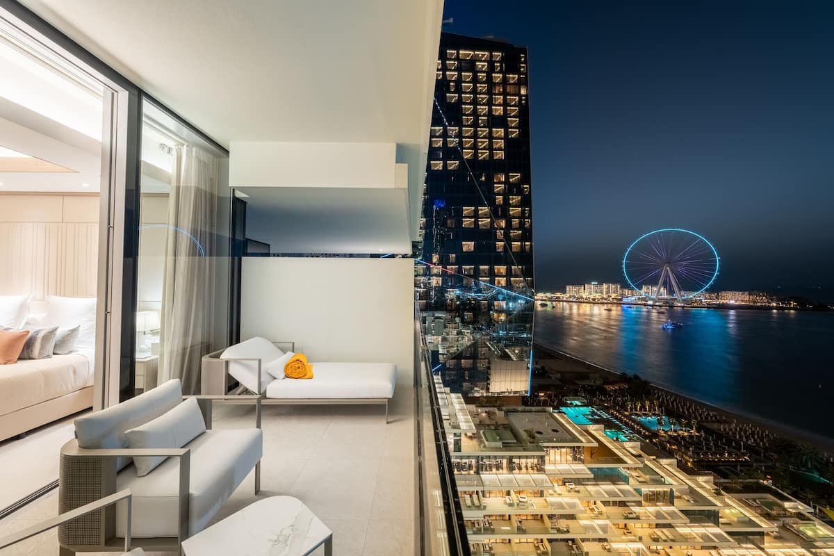 Habitación de hotel moderna con balcón que da a un paisaje urbano, incluyendo una noria y la costa.
