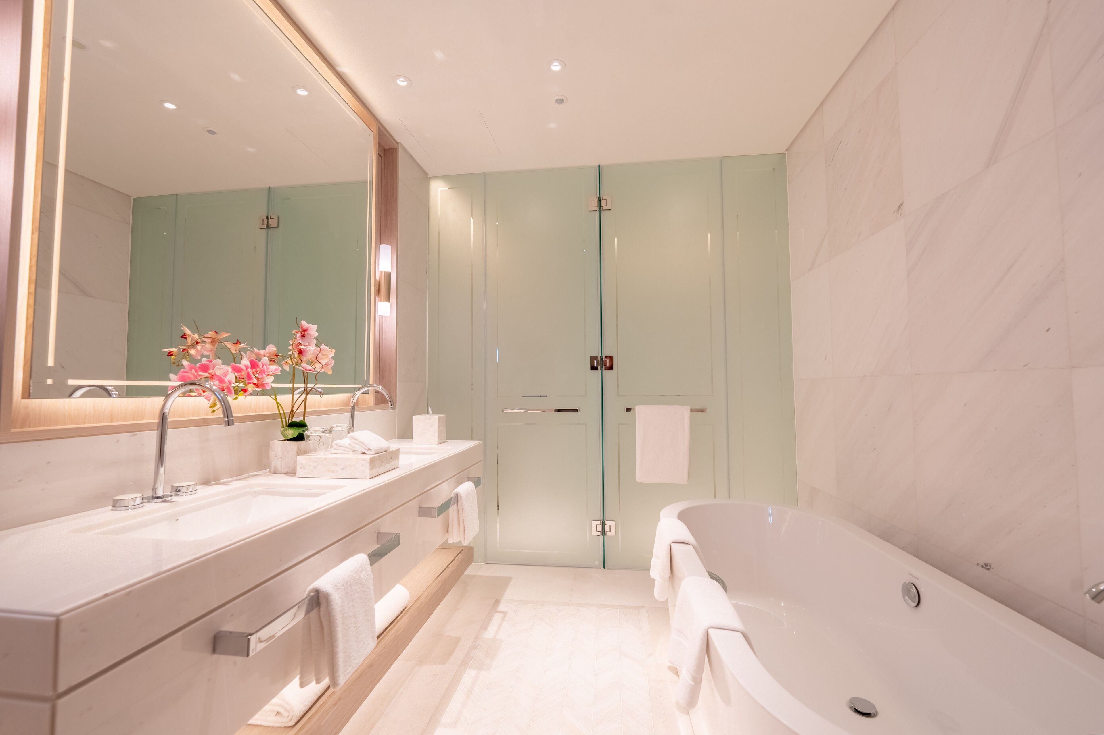 A modern bathroom with a large mirror, a bathtub, and a vanity with a sink and towel rack.