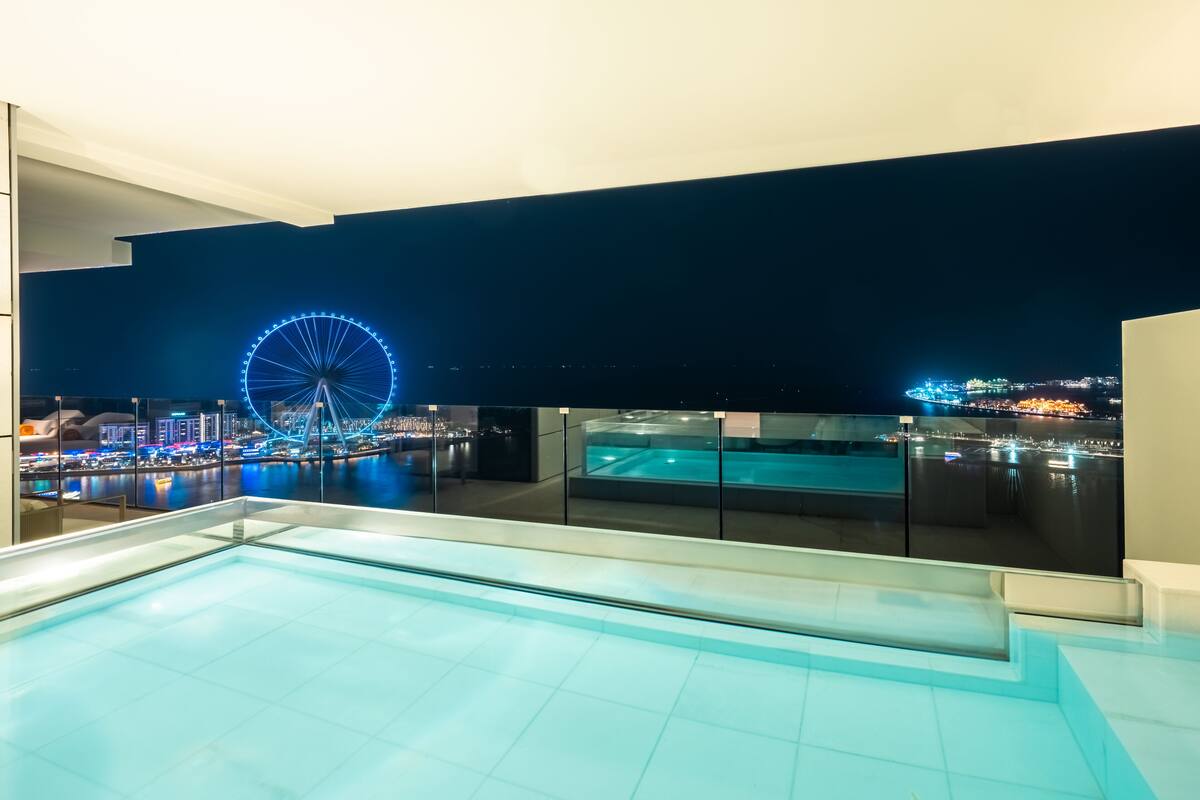 Una piscina en la azotea con vista a un paisaje urbano y una noria de noche.