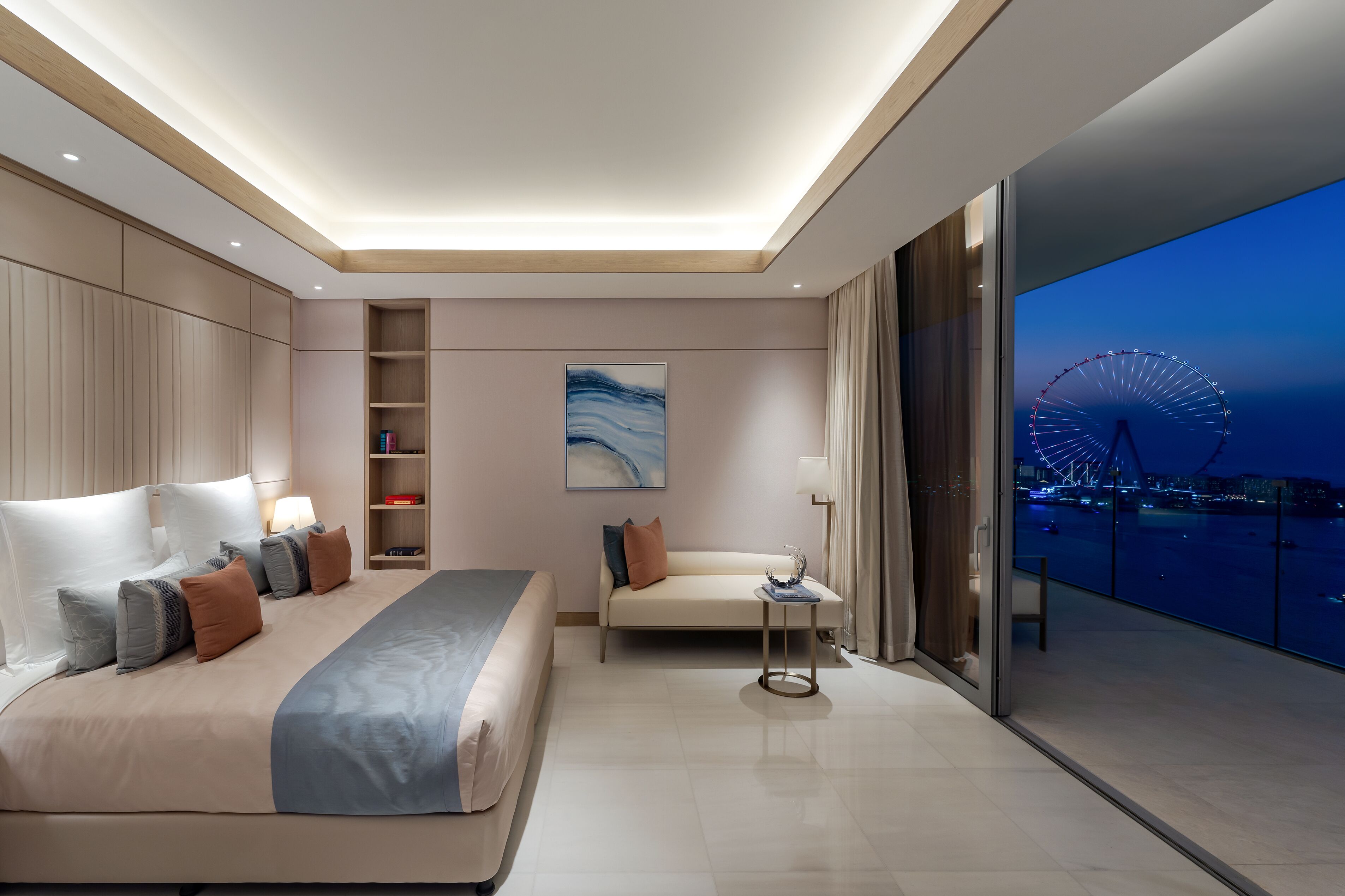 Une chambre d’hôtel moderne avec un grand lit, un canapé, une petite table et une vue sur une grande roue illuminée la nuit.