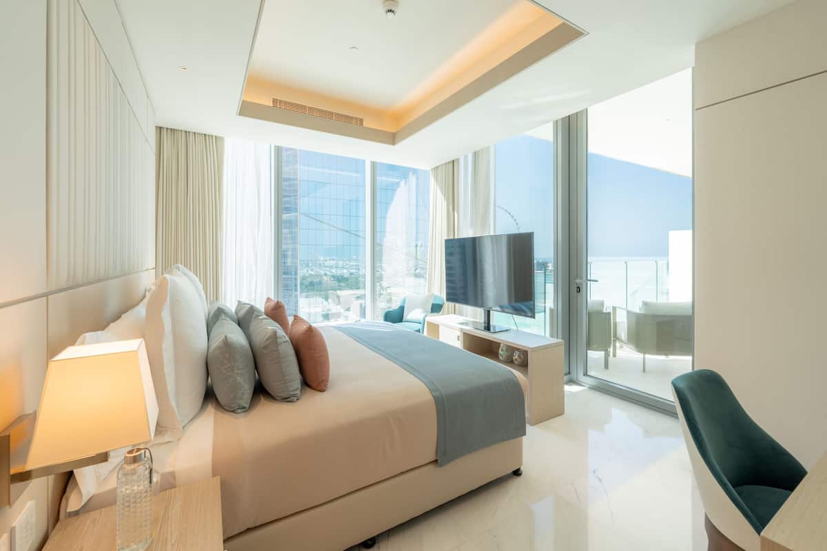 Habitación de hotel moderna con una cama grande, televisión, escritorio y vista a la ciudad.