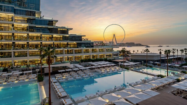 A hotel with a large pool, sun loungers, and a Ferris wheel in the background. -  FIVE LUXE (Dubai)